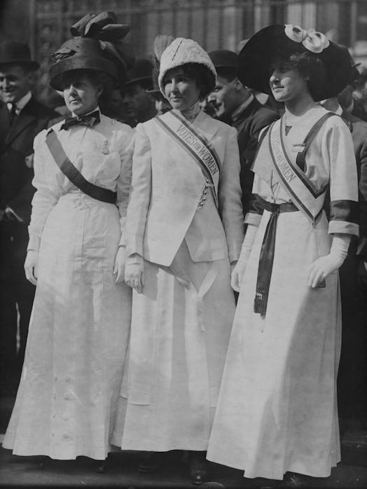 Three suffragettes posing together wearing white in a black-white photograph