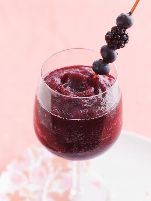 A blueberry and blackberry wine slushie sits on a pink tablecloth, and has berries coming out of it.