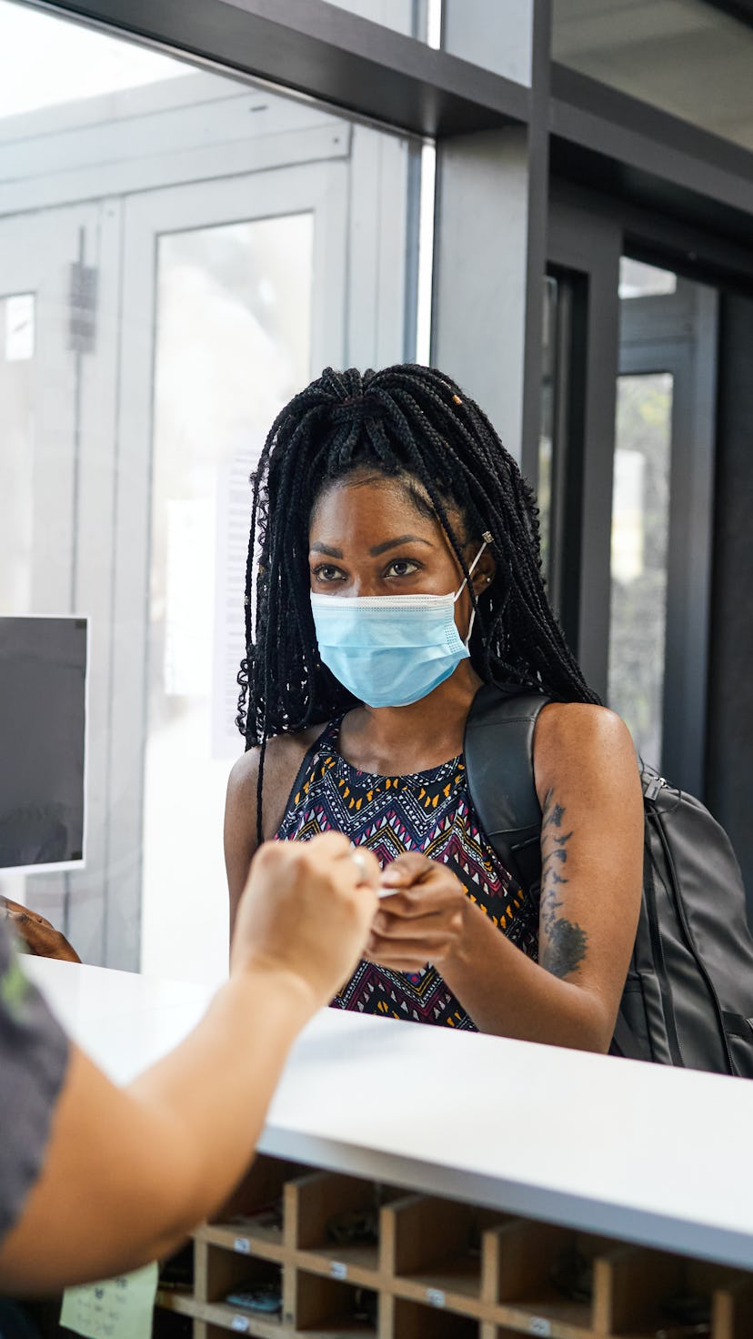 A person with natural hair wears a mask while she checks in to her gym. Even if you feel safe going ...