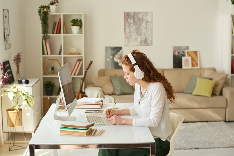 A young woman with curly, red hair sits at an organized desk in her home office.