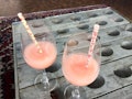 Two pink wine slushies sit on a table with floral straws stuck in them. 