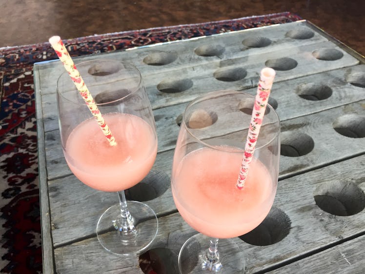 Two pink wine slushies sit on a table with floral straws stuck in them.