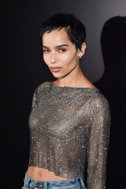 Zoë Kravitz posing side-profile on the red carpet wearing a see-through rhinestone top and a black p...