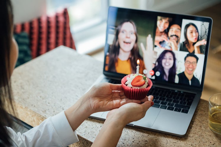 A young woman shows off her birthday cupcake to her friends who she's video chatting with.