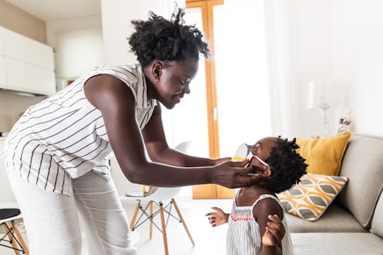 mom helping toddler girl with face mask