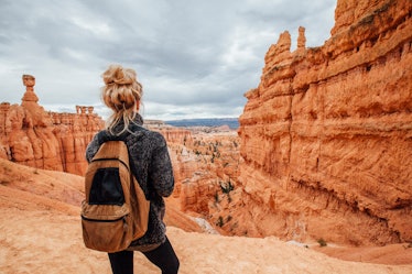 A young woman with blonde hair stands over a canyon in Bryce Canyon National Park with her backpack.