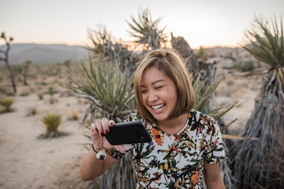 A young Asian woman laughs while looking at a picture on her phone in Joshua Tree National Park.