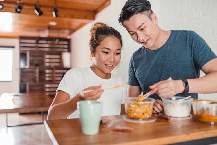 A young Asian couple enjoys takeout food in their kitchen for a fall dinner date at-home.