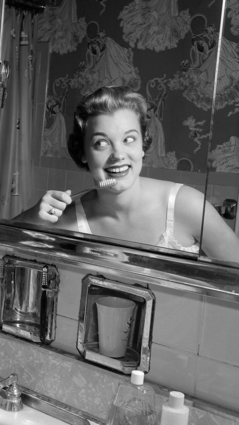 A woman brushes her teeth in the mirror. A dentist told the new york times how much pandemic stress ...