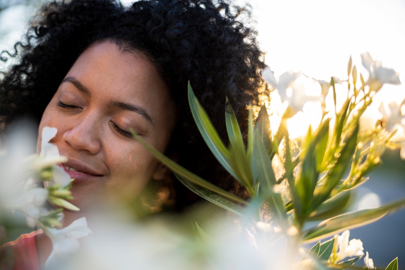 A woman with natural curly hair smells a flower. Here's what covid does to your sense of smell.