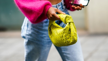 A woman in jeans and a pink sweater carrying a neon green croissant bag