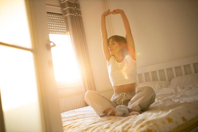 A woman stretches in her bedroom in the morning. Morning stretching routines can help people get the...