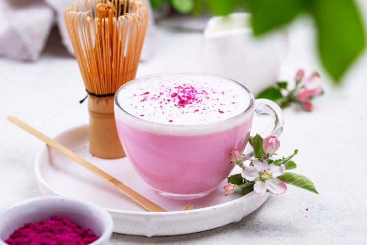 A pink latte sits on a white table with flower garnishes. 