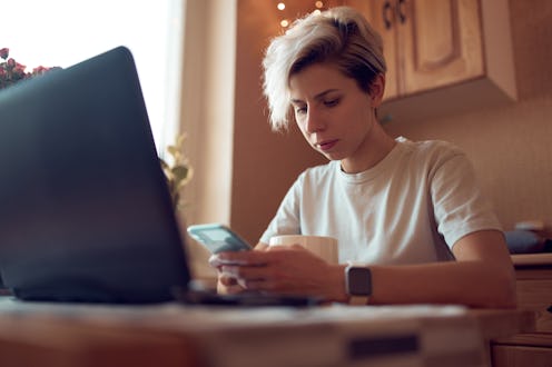A person texts at their kitchen table with their laptop open in front of them. Millions of people ha...