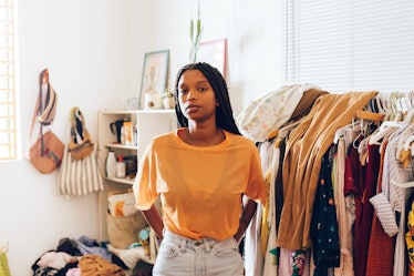 A young Black woman stands in front of a rack of trendy clothes in her home.