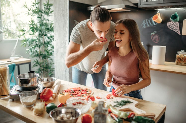 A happy couple goofs around while making baguette pizza in their bright kitchen.