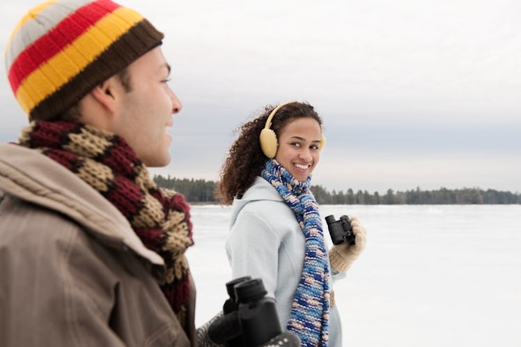 A young couple takes a winter hike with binoculars on a cloudy day.