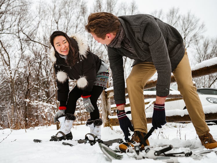A happy couple adjusts their snowshoes in the snow.