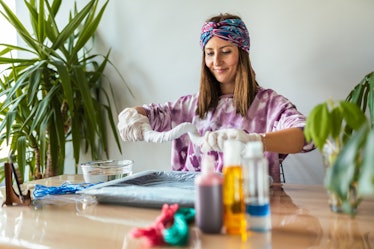 A young woman bleach tie-dyes clothes in her living room. 