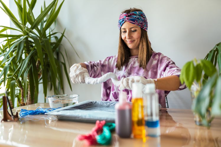 A young woman bleach tie-dyes clothes in her living room.