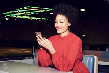 A young Black woman looks at her phone while sitting in a diner at night.