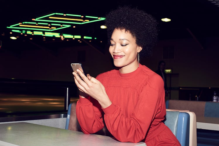 A young Black woman looks at her phone while sitting in a diner at night.