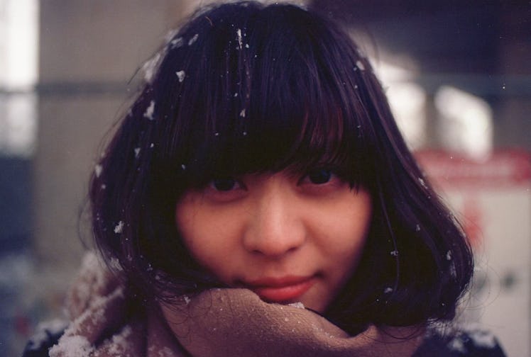 A woman in black bangs smiles at the camera with a snow peppering her hair.