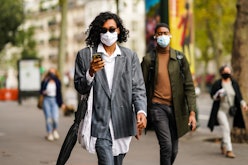 A woman walking down the street, wearing a face mask and scrolling through clothing on a delivery ap...