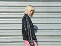 A blonde woman looks to the side while showing off her haircut and wearing a leather jacket and brig...