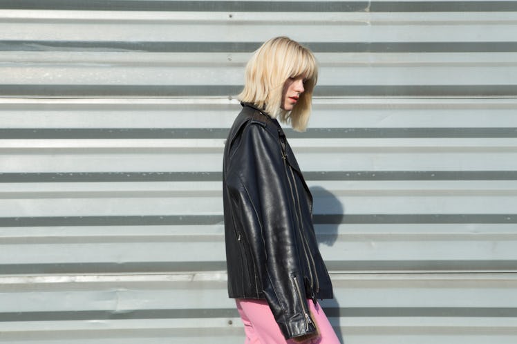 A blonde woman looks to the side while showing off her haircut and wearing a leather jacket and brig...