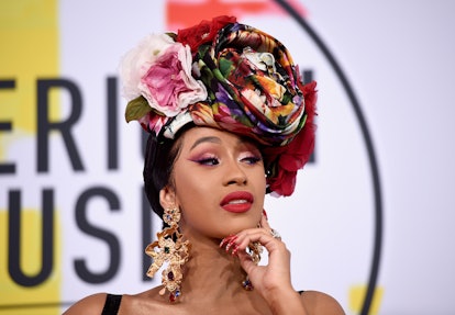 Cardi B wears a floral headpiece while standing on the red carpet at an event. 