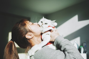 A young woman kisses her cat on a sunny afternoon in the winter.