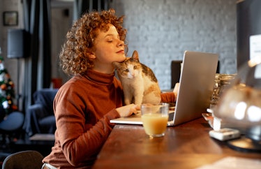 A young woman types on her laptop while hanging out with her cat.