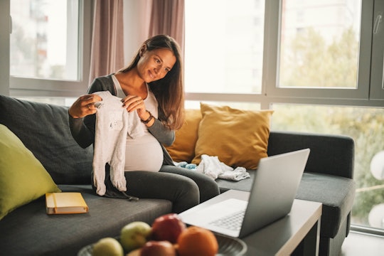 pregnant woman holding up onesie in front of laptop