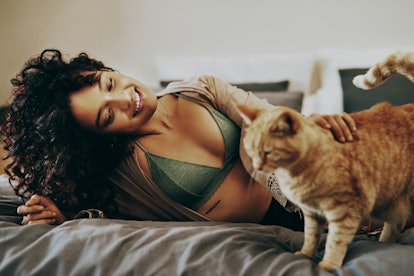 A young woman hangs out in bed and pets her cat.
