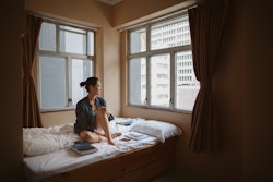 A person sits on a bed looking out the window. It's normal to feel sad, even during happy times.