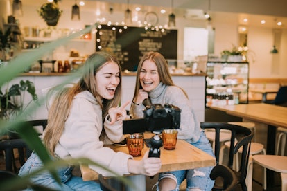 Two friends laugh and take selfies in a coffee shop.