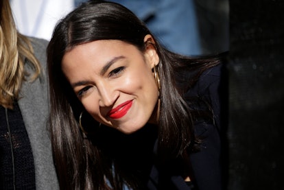Rep. Alexandria Ocasio-Cortez smiling in a black suit and red lipstick