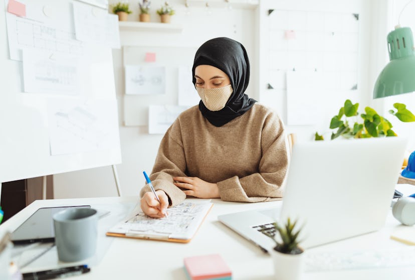 A woman wearing hijab wears a mask at an office. Can your job force you to be vaccinated before goin...