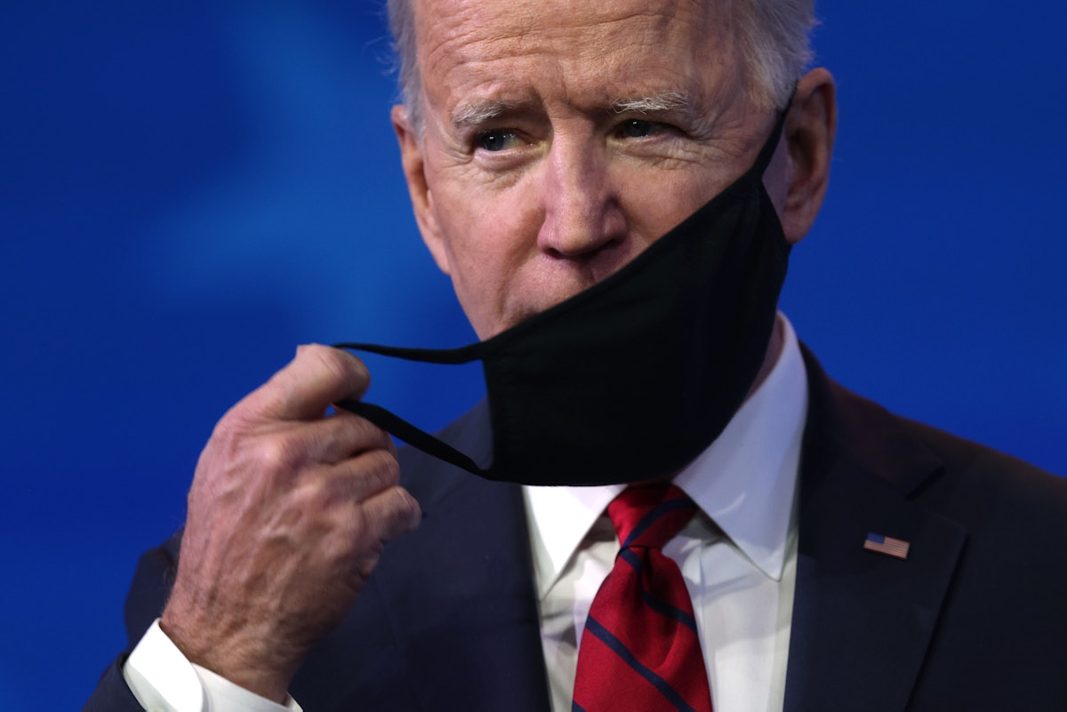 Biden wearing black mask in front of blue background.