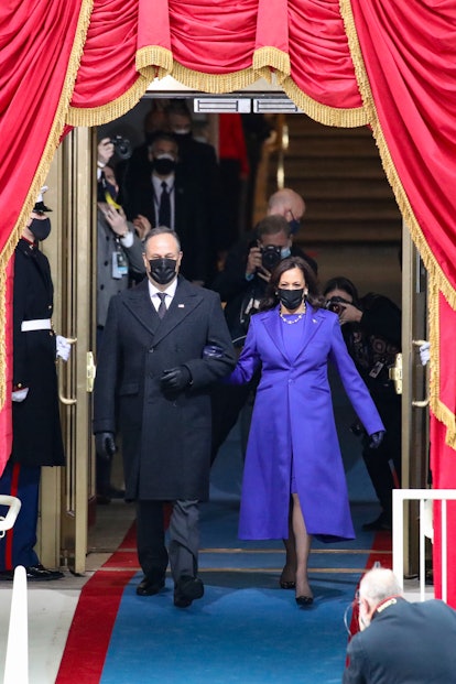 Kamala Harris in a blue dress and blue coat, walking hand in hand with Douglas Emhoff who is wearing...
