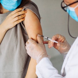 A person wearing a blue surgical mask receives a covid-19 vaccine.
