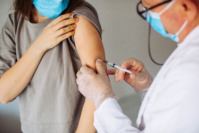 A person wearing a blue surgical mask receives a covid-19 vaccine.