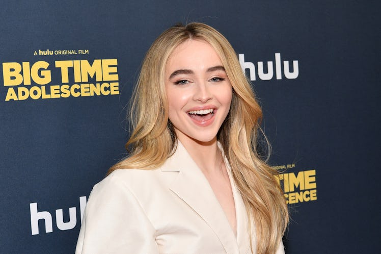 Sabrina Carpenter smiles on the red carpet in a white suit.