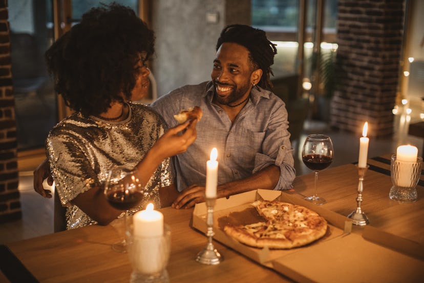 A man and a woman eating pizza with two candles on the table to make Valentine's Day feel romantic a...