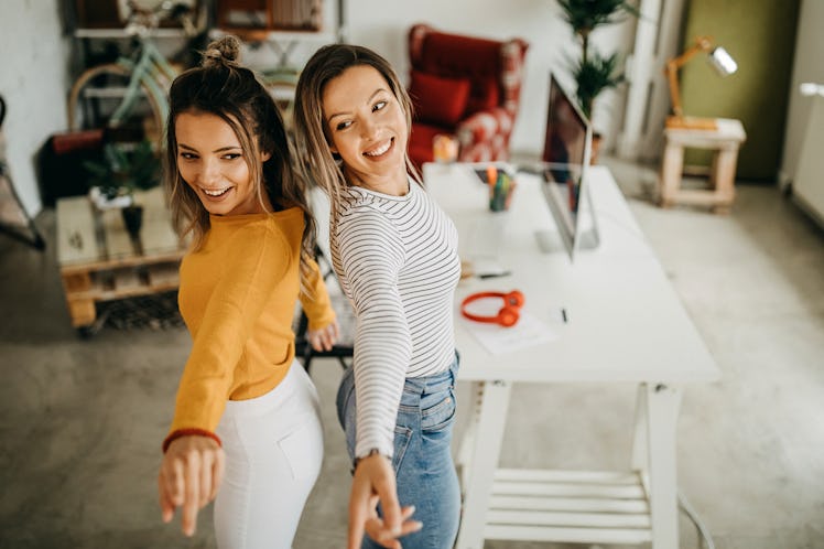 Two happy roommates dance around in their bright living room on Galentine's Day.