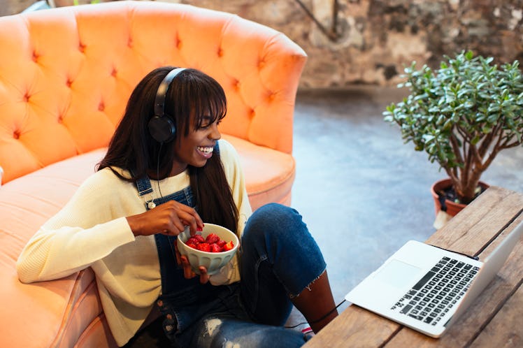 A young Black woman eats strawberries while video chatting and playing games with her friends on Gal...