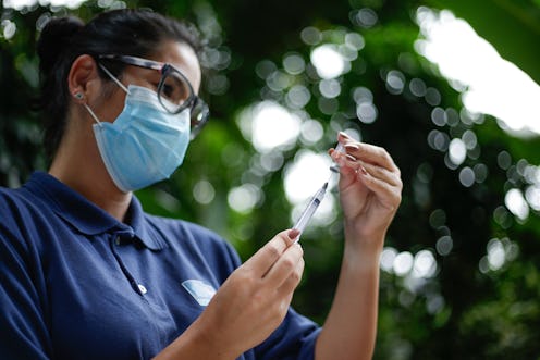 A person wearing a mask examines a syringe. Volunteering to help with COVID vaccine distribution can...
