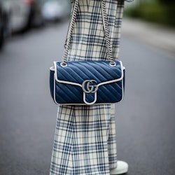 A person wearing plaid pants and holding a blue Gucci Marmont bag.