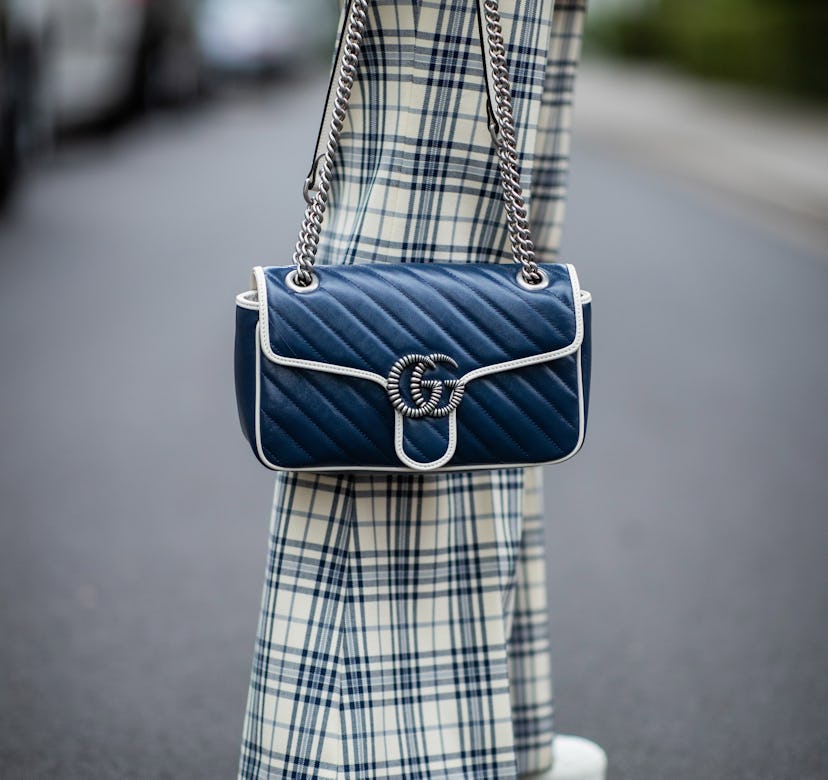 A person wearing plaid pants and holding a blue Gucci Marmont bag.